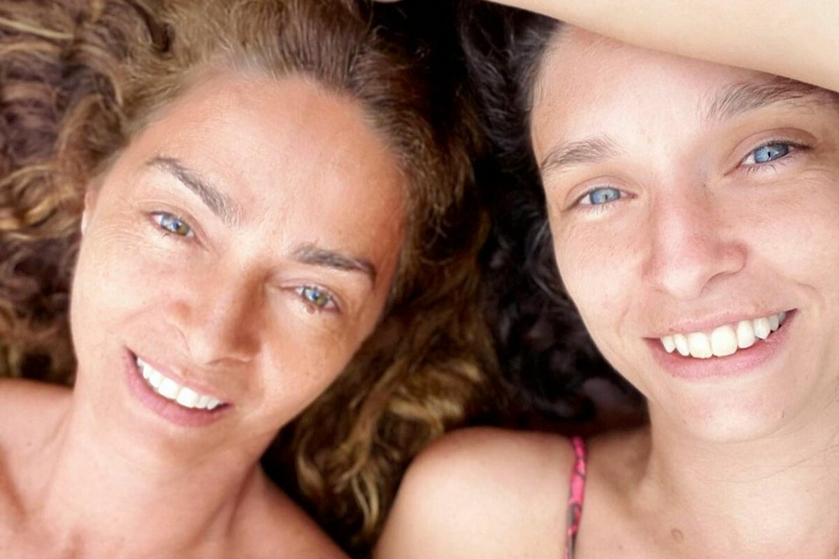 Claudia Ohana deitada ao lado da filha, Dandara Guerra ambas sorrindo